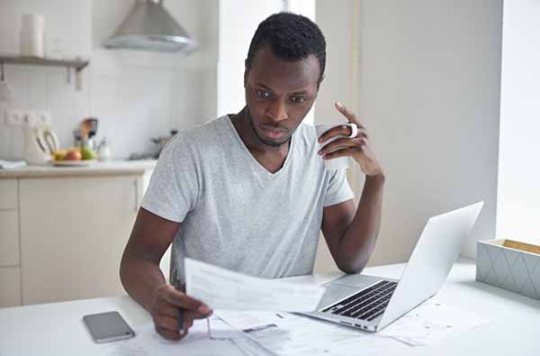 Man Reviews Electric Bill Costs in Front of Laptop