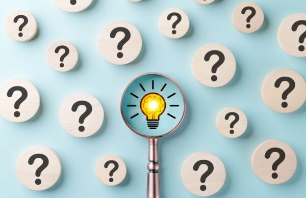 An image of a magnifying glass focusing on a lightbulb surrounded by question marks. 